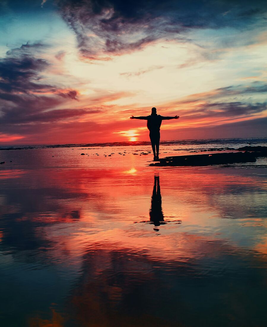 Silhouette bras ouverts face à un lever de soleil coloré sur l'eau, image de l'éveil spirituel